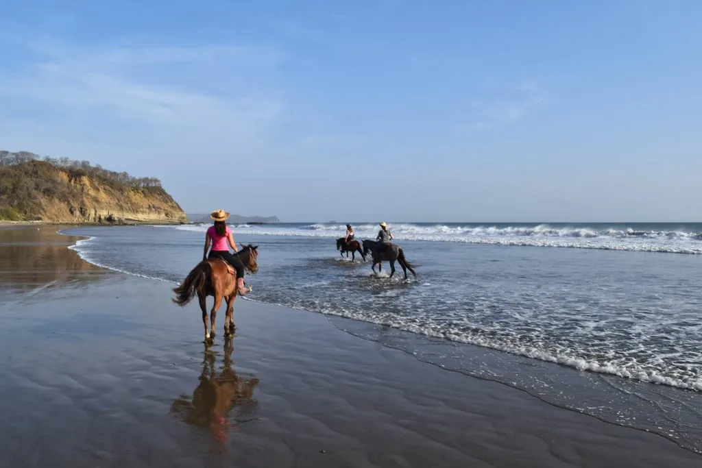 kate storm in a pink shirt horseback riding in nicaragua on a beach
